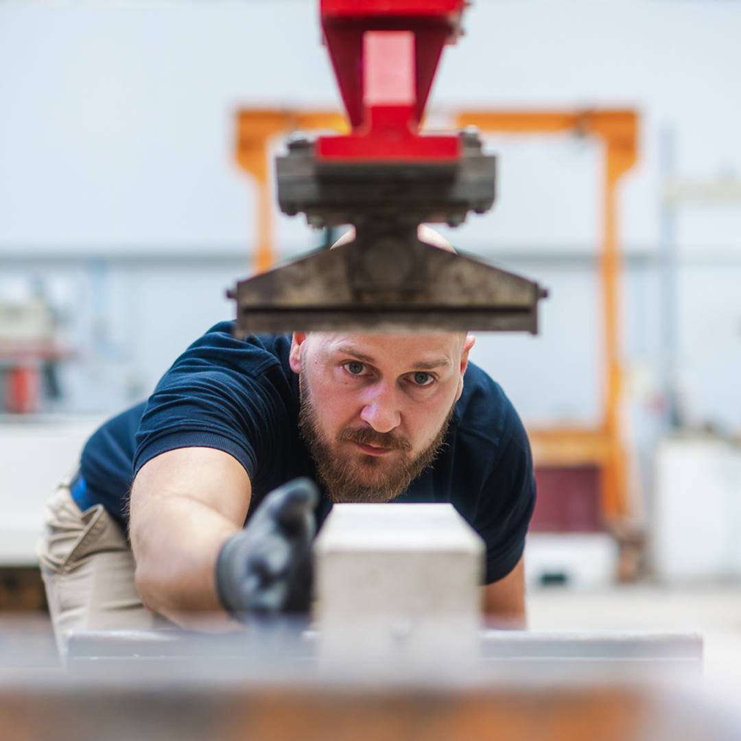 Kiwa laboratory employee operating industrial machinery in a workshop, focusing intently on a task, wearing a glove and casual work attire